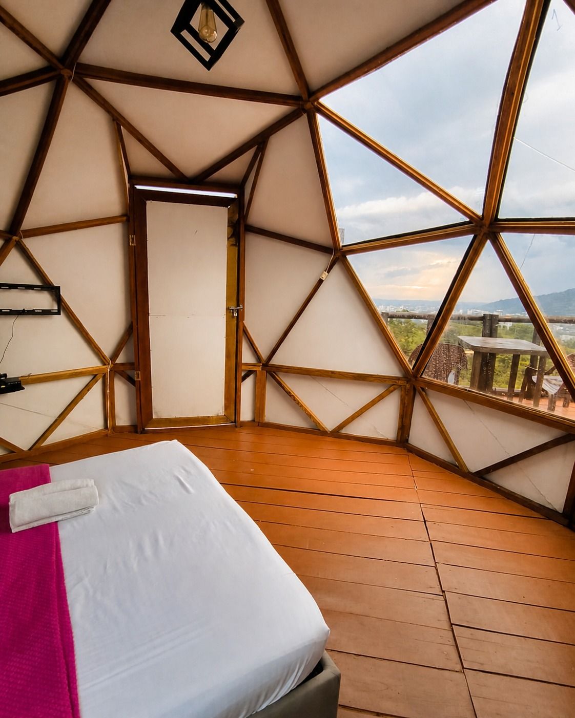 Cama junto a los ventanales de un domo, con montañas al fondo.